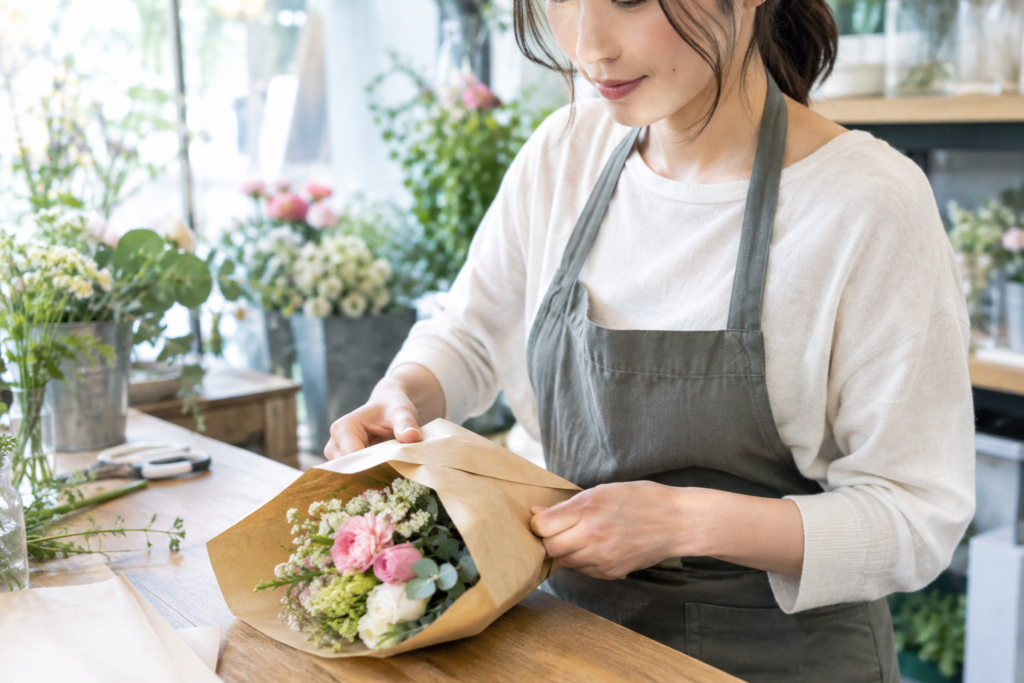 エプロン姿の女性がテーブルで花束をラッピングしている
