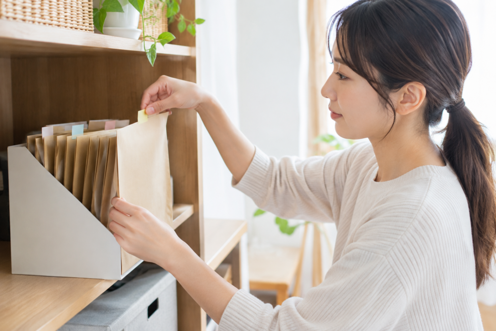 棚の書類ケースから封筒を取り出して整理する女性