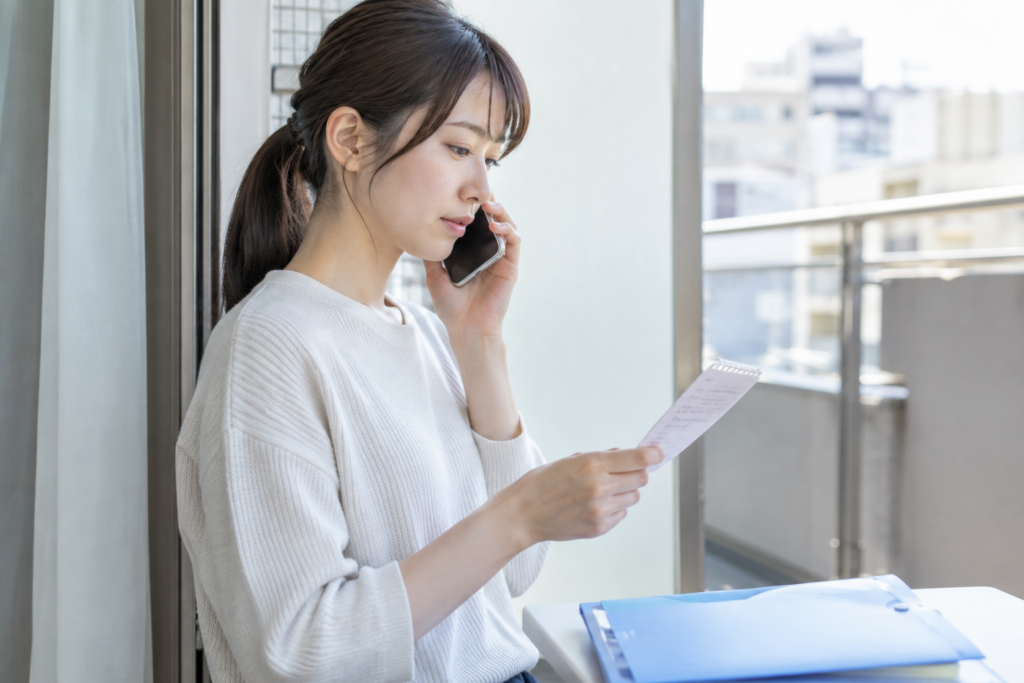 女性が電話をしながら紙の資料を確認している