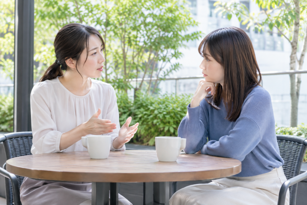 屋外のカフェで向かい合い、話しながら相談している女性2人
