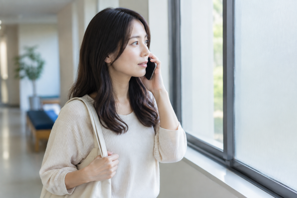 窓際でスマートフォンを耳に当て、外を見ながら通話する女性