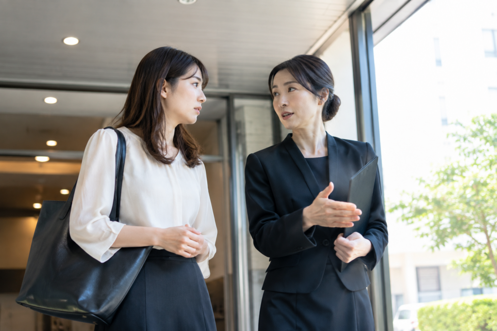 屋内の通路で、女性2人が歩きながら話し合っている