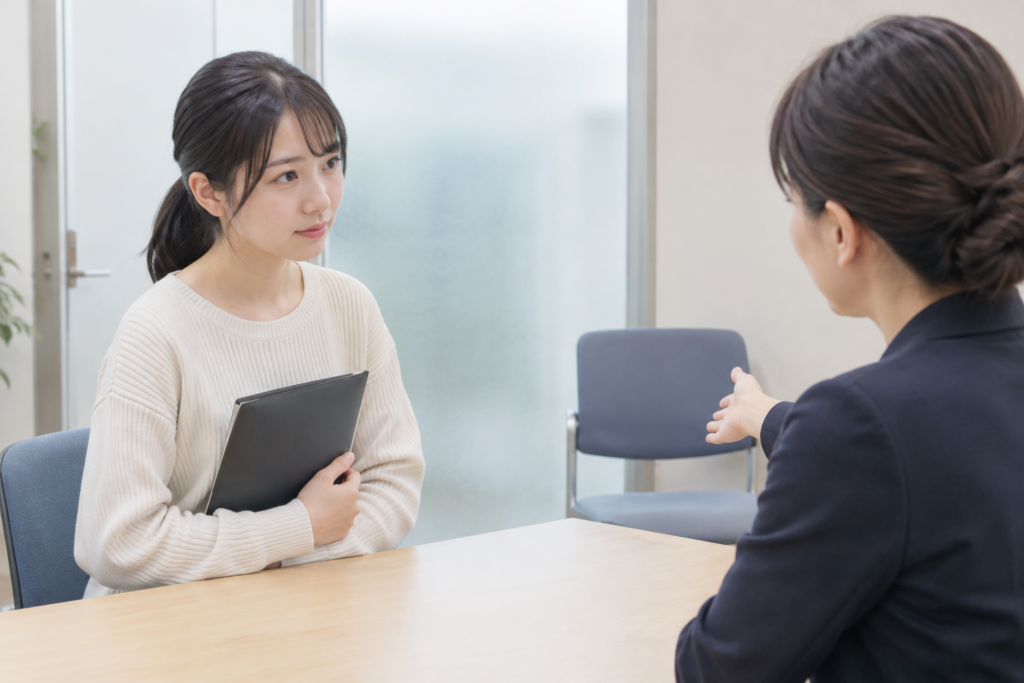面談室で女性が書類を抱えて相談相手と向かい合って話している