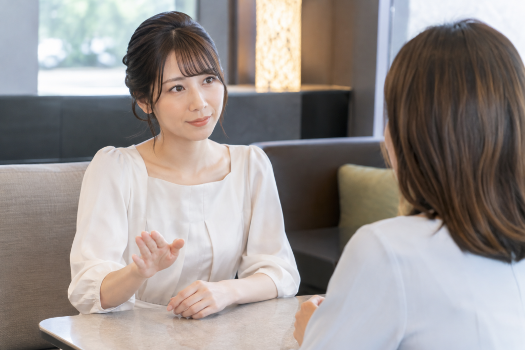 カフェの席で女性が向かいの相手に説明しながら相談している